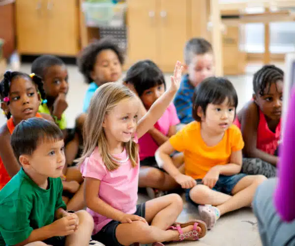 Groupe d’enfants attentifs assis au sol dans une salle, participant à une animation pédagogique dans un centre de loisirs