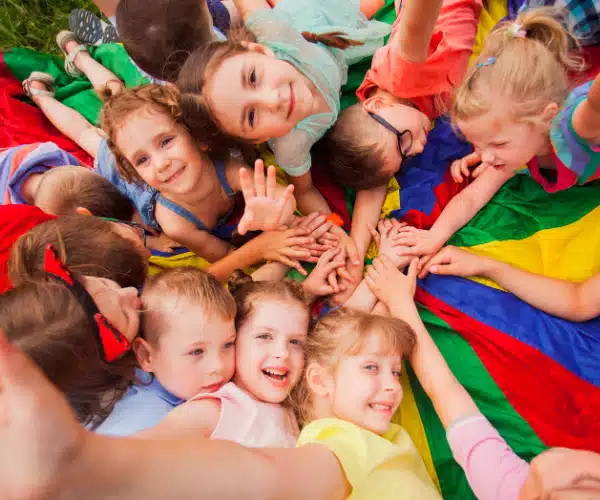 Groupe d’enfants souriants jouant ensemble sur une bâche multicolore lors d’une activité ludique en centre de loisirs