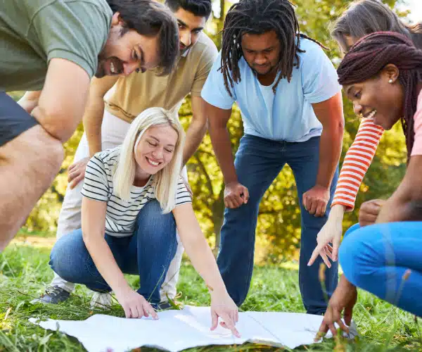 Groupe de jeunes adultes en plein air, en train de lire une carte ensemble lors d’une activité associative immersive