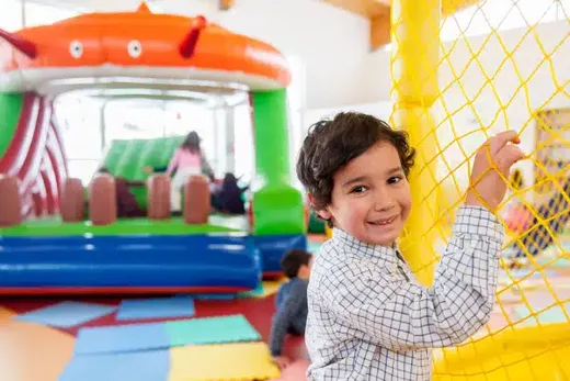 Un enfant sourit en tenant un filet dans une aire de jeu colorée.